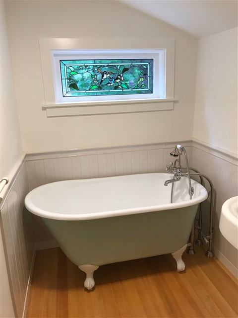 Clawfoot tub with beadboard wainscot and a stained-glass window