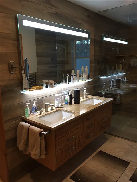 Floating double vanity with wood-look tile walls and a lit mirror
