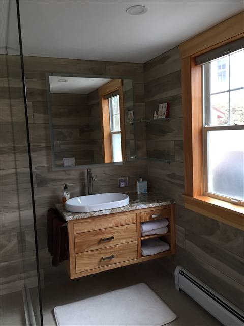 Floating wood vanity with a vessel sink and wood-look tile walls
