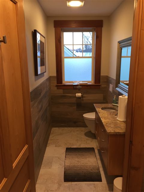 Narrow bathroom with wood-look tile wainscot and natural wood trim