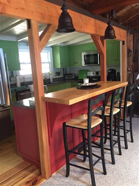 Kitchen with green cabinets, timber posts, and a red island with a wood bar top